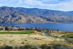 Ein Ort am Ende des Kamloops Lakes mit grünen Feldern vor trockenen Bergen.